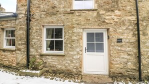 Un bâtiment en pierre doté de deux fenêtres et d’une porte, une enseigne indiquant « East House », et un petit jardin agrémenté d’un sentier en pierre.