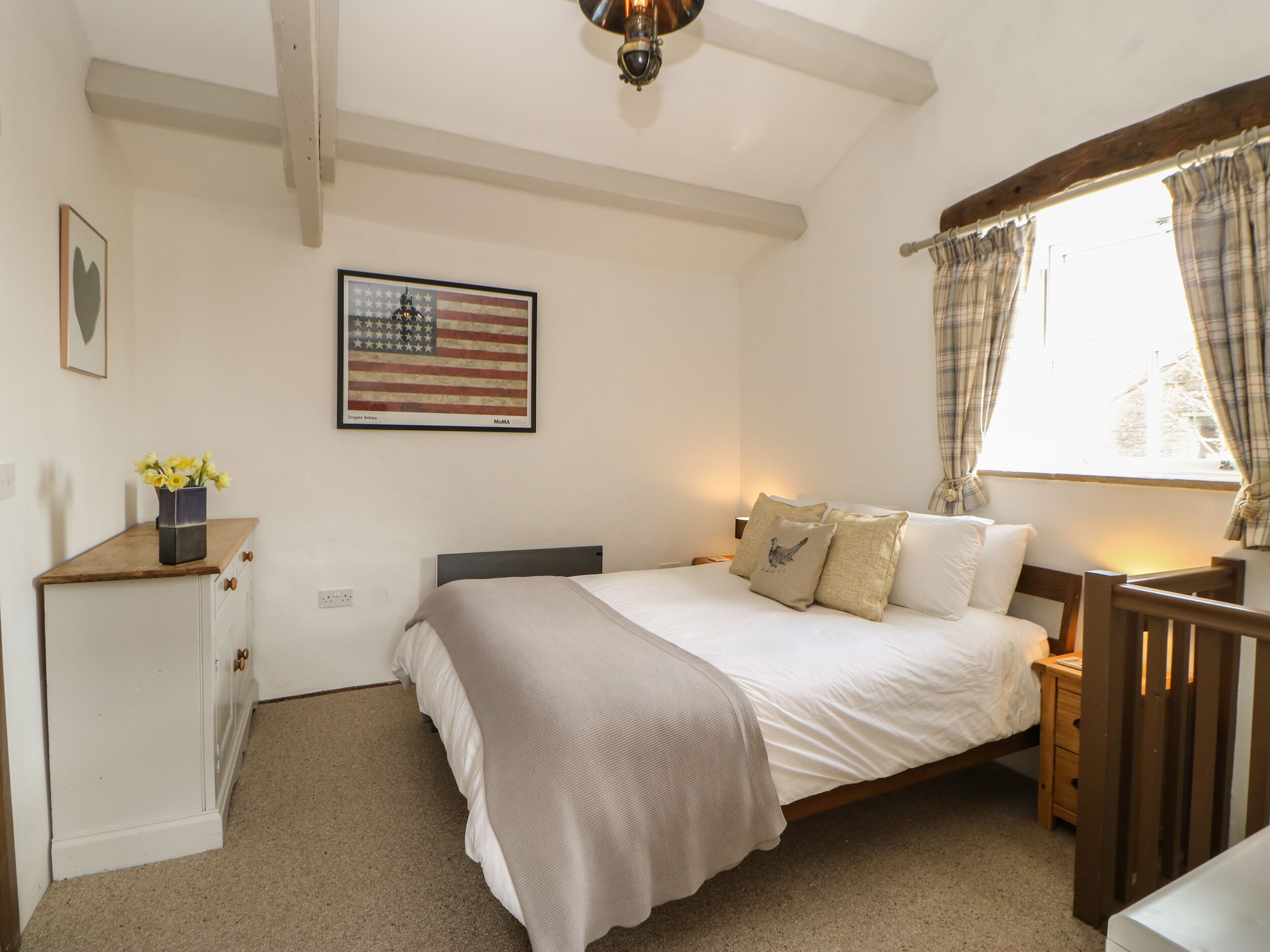 A bedroom with a bed, a nightstand, a dresser, a window with curtains, and an American flag on the wall.