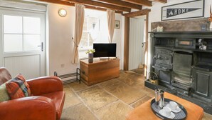 Un salon chaleureux avec un sol en pierre, un canapé en bois, une télévision et une cheminée.
