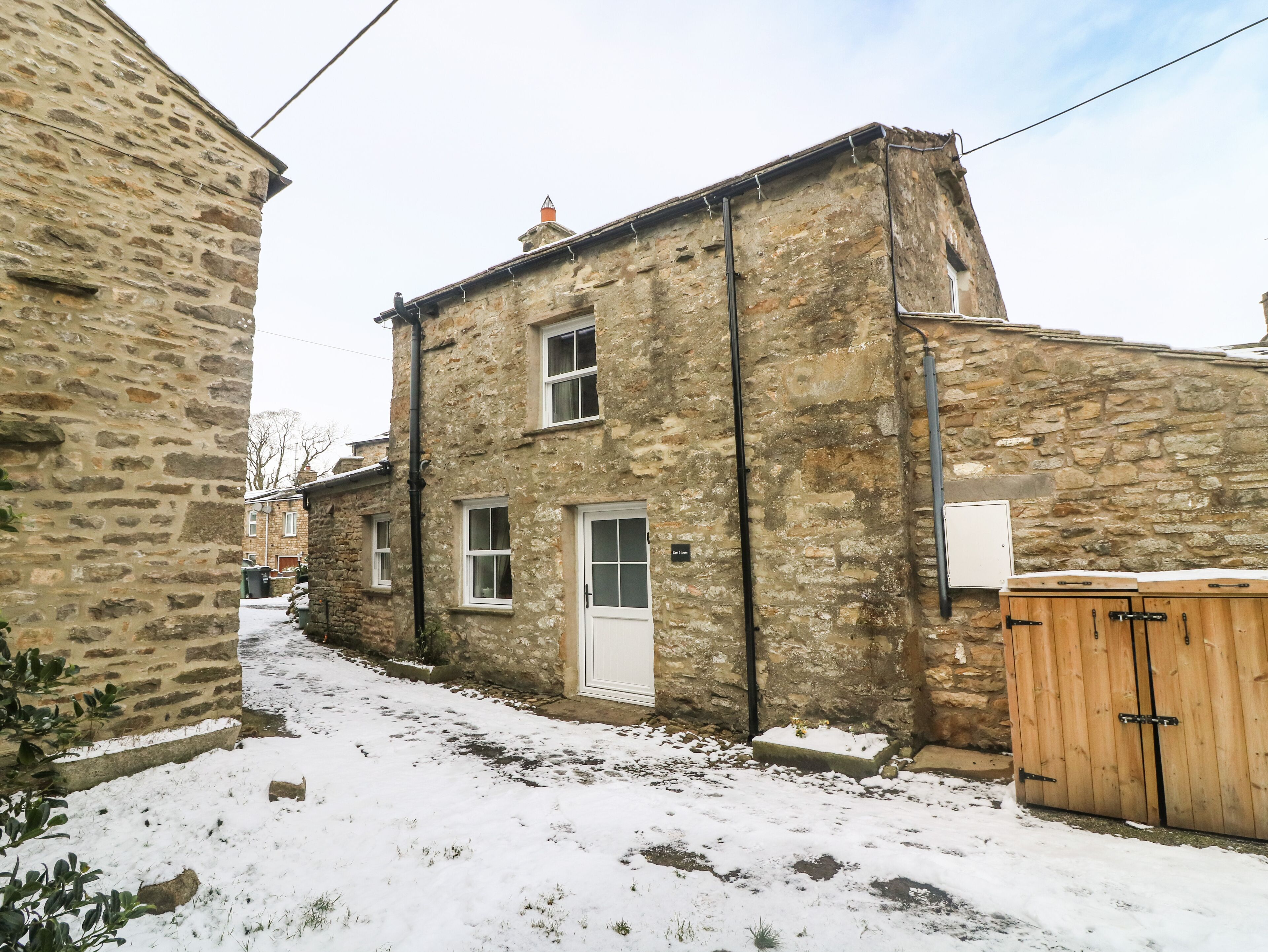 A stone building with a white door and windows, a wooden gate, and a snow-covered ground.