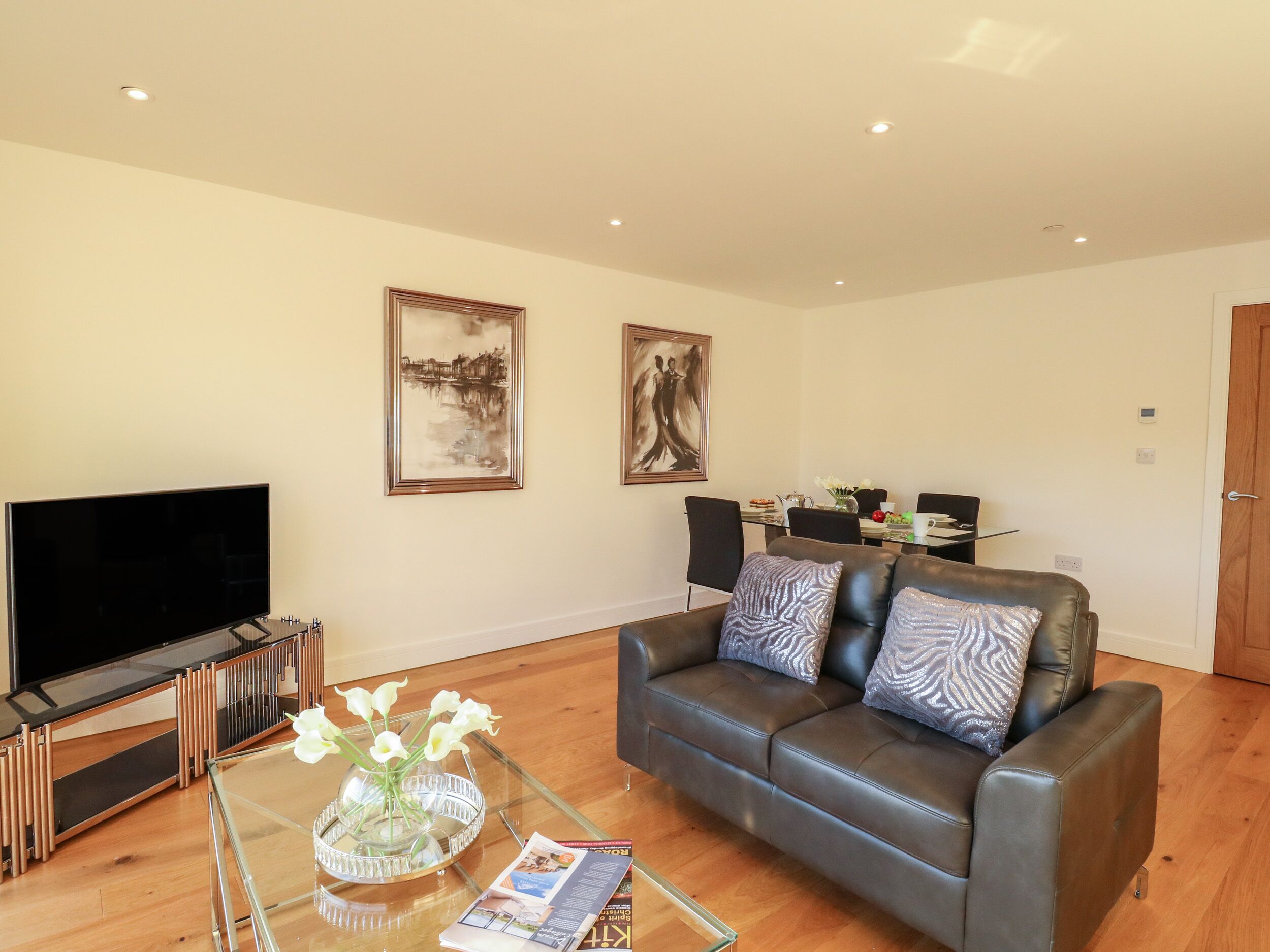 A living room with a leather sofa, a glass coffee table, a flat-screen TV, and two framed artworks on the wall.