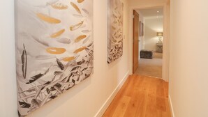 A hallway with wooden flooring and two large abstract paintings on the walls. - Harbourside Haven Apartment 4 (Weymouth)