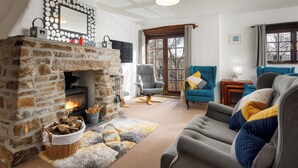 Ein gemütliches Wohnzimmer mit Kamin aus Stein, blauem Sessel, grauem Sessel und grauem Sofa mit bunten Kissen.