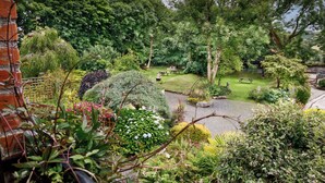 Ein Garten mit Rasenfläche, Picknicktischen und unterschiedlichen Sträuchern und Bäumen.