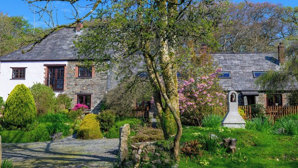 Ein traditionelles Steinhaus mit einem gepflegten Garten, einschließlich verschiedener Sträucher und blühender Pflanzen.