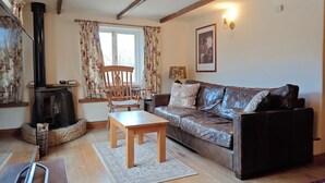 Een gezellige woonkamer met een bank, een houten tafel, een open haard en een raam met gordijnen.