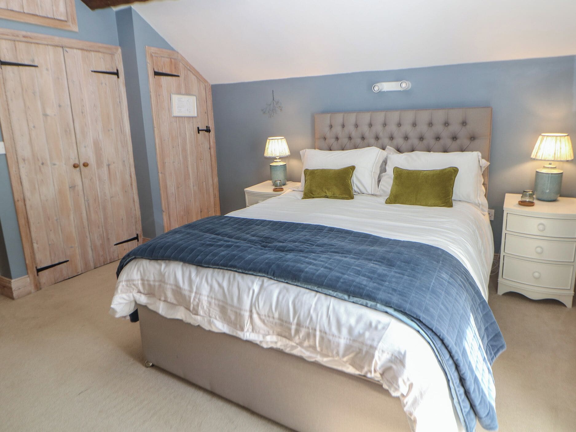 A bedroom with a large bed, two bedside tables with lamps, and a wardrobe.