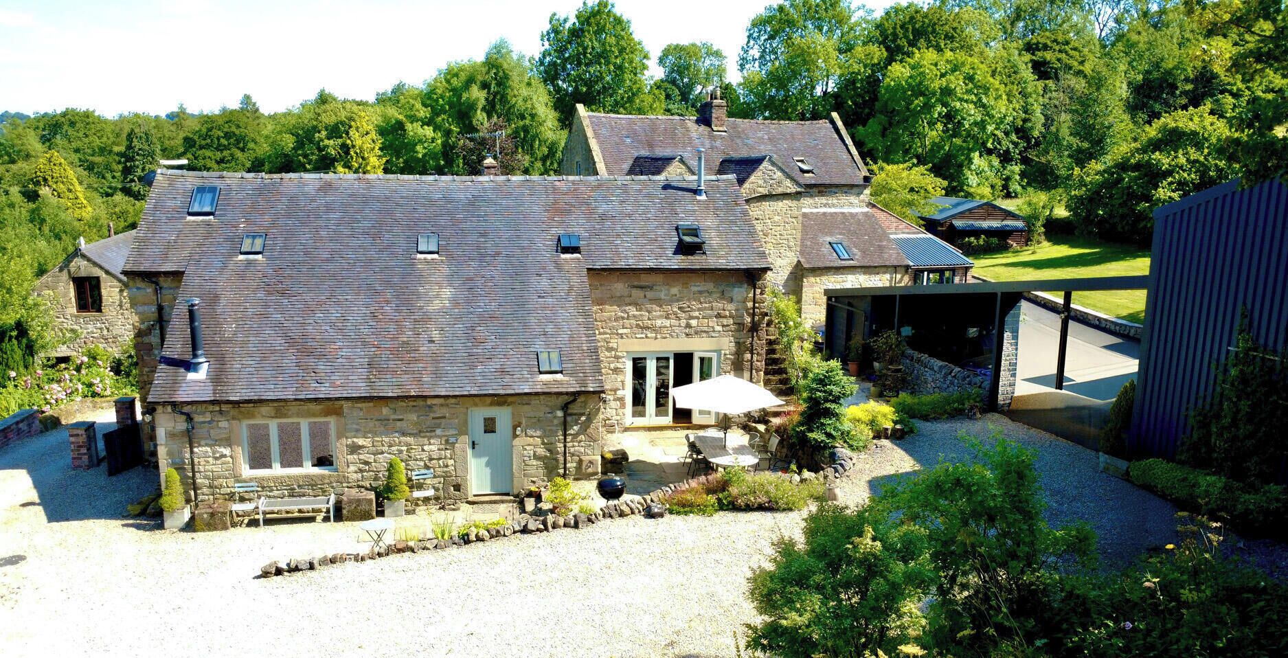 A stone house with a sloped roof, a covered porch, and a gravel driveway.