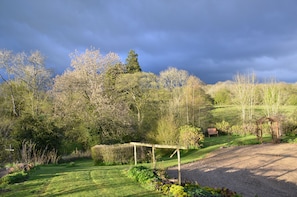 A rural landscape with a gravel path, a wooden pergola, and a bench.