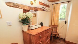 Een houten dressoir met lades, een spiegel en een kamerplant. Ook een houten stoel en een kapstok met hangers.
