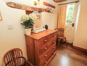 A wooden dresser with drawers, a mirror, and a potted plant. There is a wooden chair and a coat rack with hangers.
