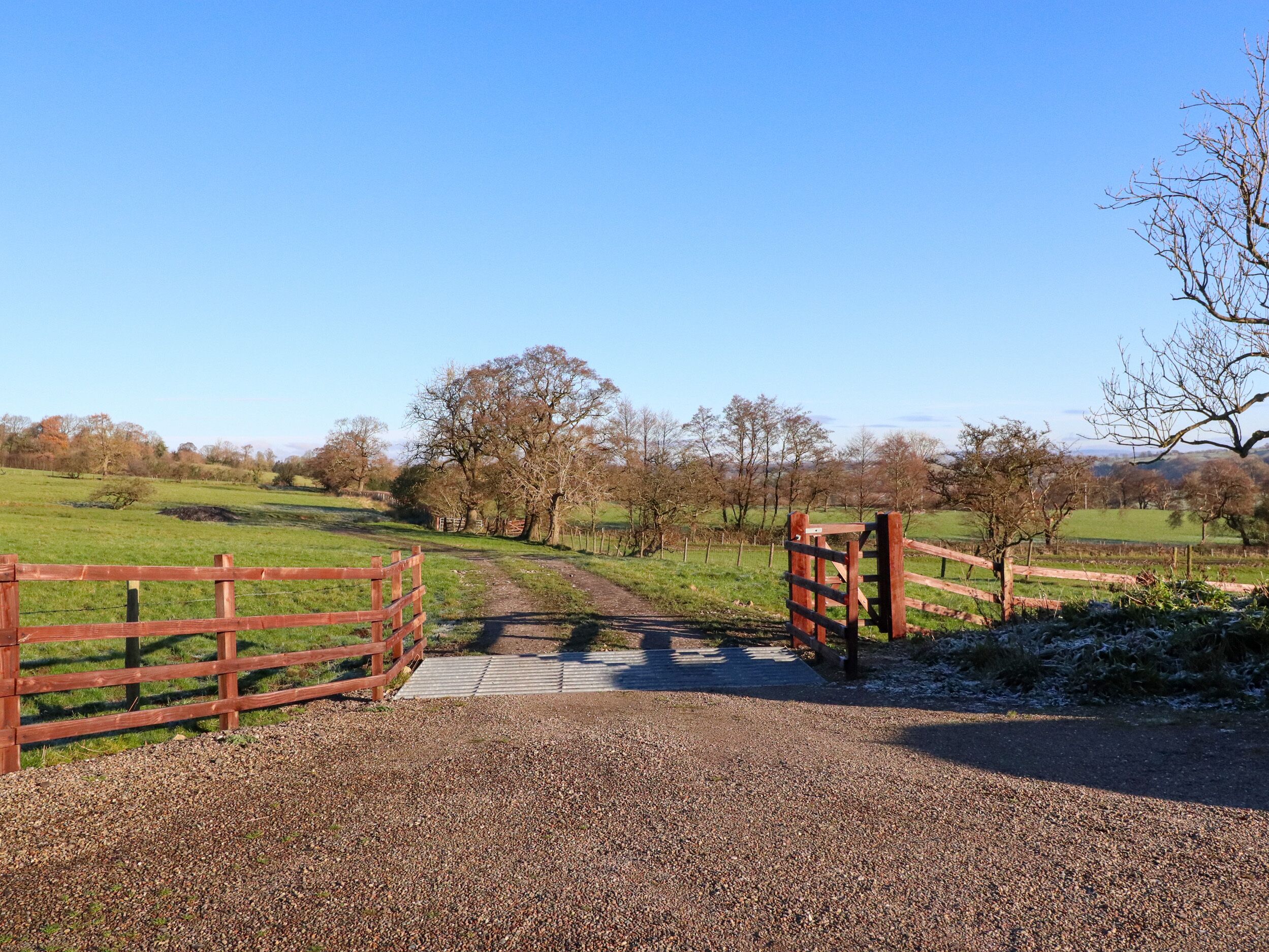 A gravel path leading through a wooden gate into a rural landscape with trees and open fields.