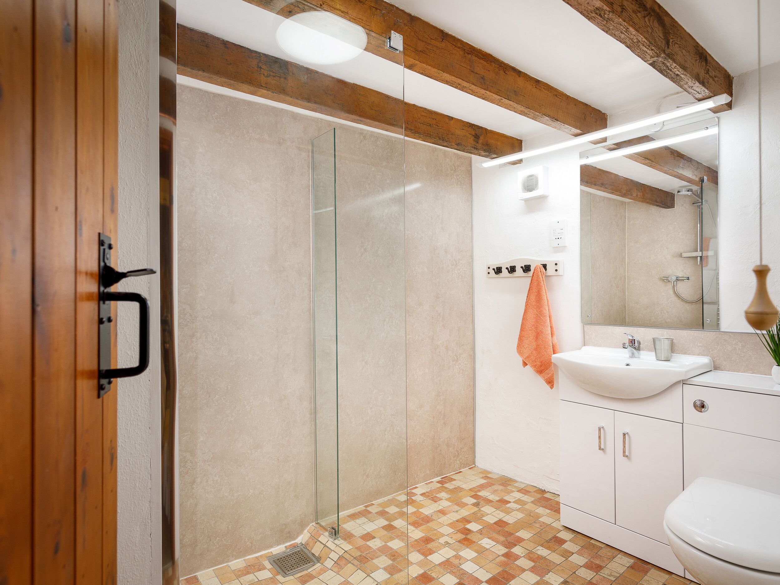 A modern bathroom with a glass shower enclosure, a white sink, and a tiled floor.