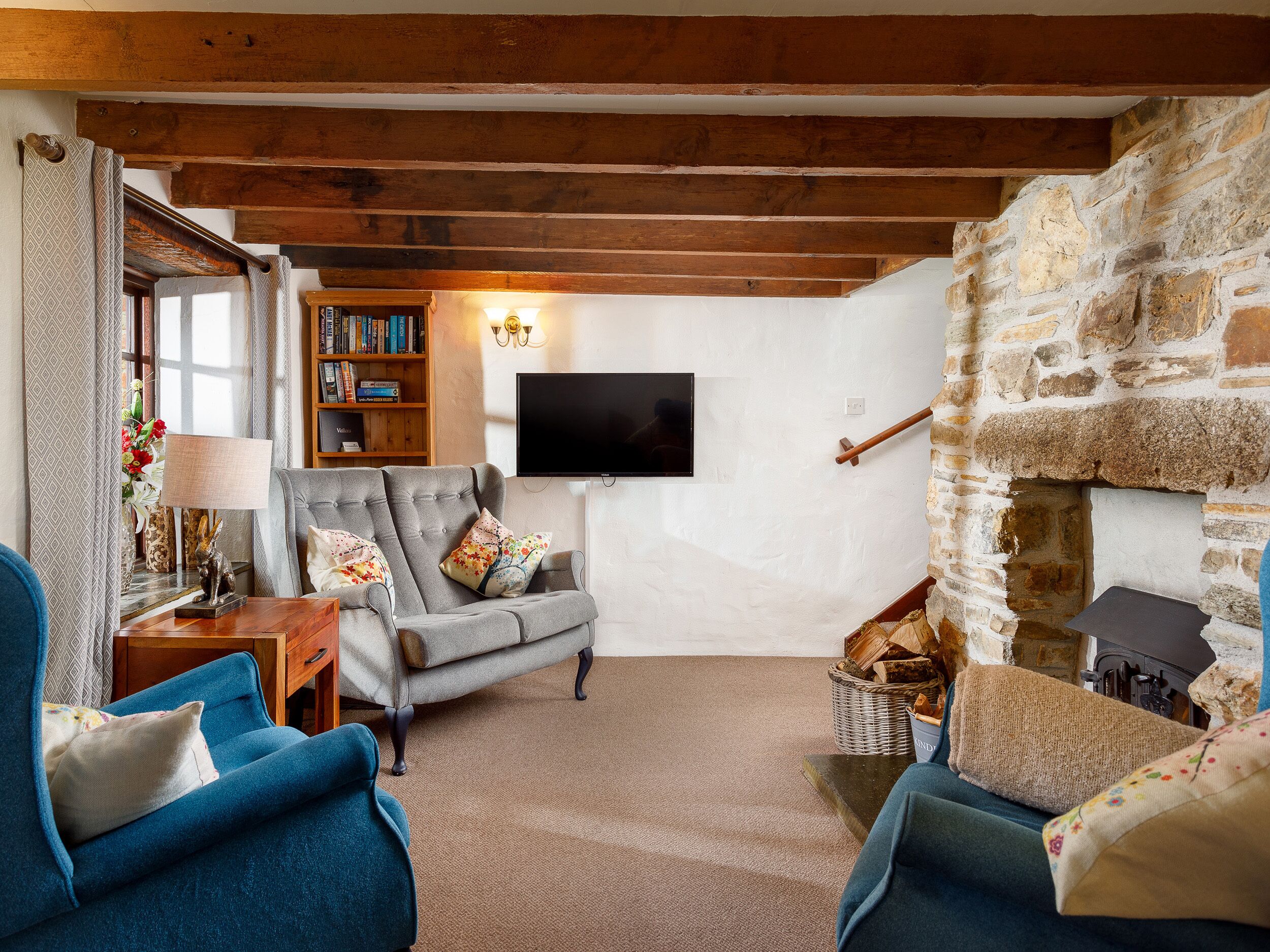 A cozy living room with a stone fireplace, a television mounted on the wall, and a bookshelf filled with books.
