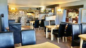 A restaurant interior with stone walls, wooden tables, and black leather chairs. - Heather (Ruthin)