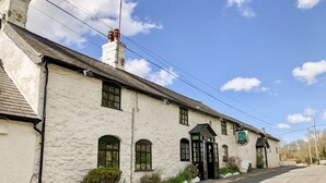 A white building with a black door and windows, a chimney, and a signboard. - Heather (Ruthin)
