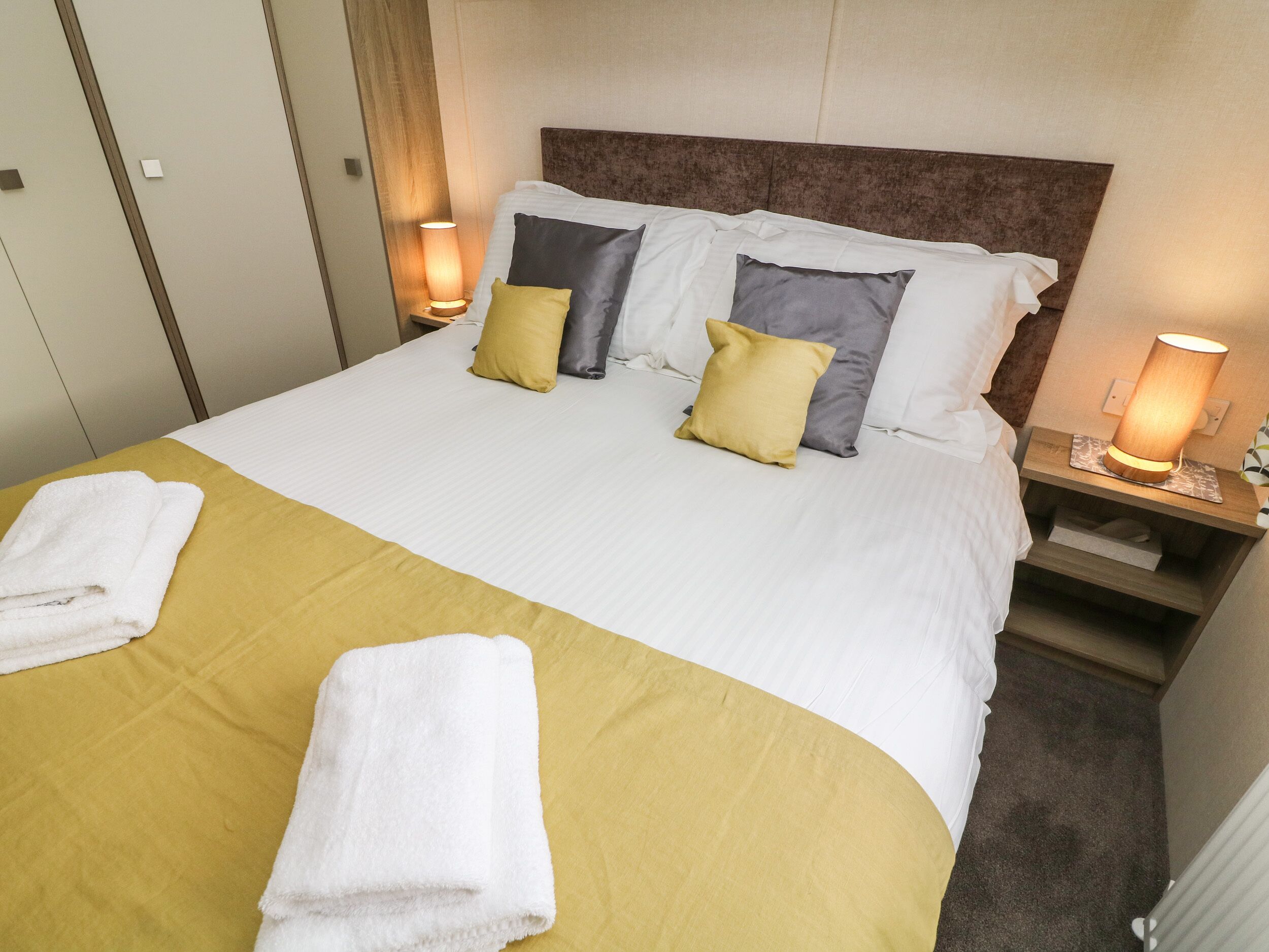A neatly made bed with a yellow bedspread, two pillows, and two bedside lamps.