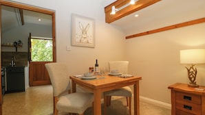A dining area with a wooden table, two chairs, a lamp, and a kitchen visible in the background. - The Coach House Apartment (Tewkesbury)