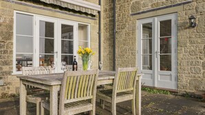 A stone building with a wooden table and chairs, a bottle of wine, and a vase of yellow flowers. - Samstone (Shaftesbury)
