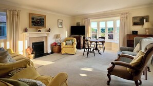 A living room with a fireplace, a television, a dining table with chairs, and a view of the outdoors through large windows. - Samstone (Shaftesbury)