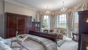 A spacious bedroom with a large bed, a sitting area with a sofa, and a wooden wardrobe. - Tal Gwynedd (Llanfairpwllgwyngyll)
