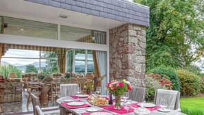 An outdoor dining area with a stone wall, wicker furniture, and a view of the landscape. - Tal Gwynedd (Llanfairpwllgwyngyll)