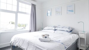A neatly made bed with a towel and a pillow, a bedside table with a lamp, and a window with curtains.