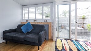A living room with a dark grey sofa, a wooden coffee table, and a large sliding glass door leading to a backyard with a wooden fence and a potted plant.