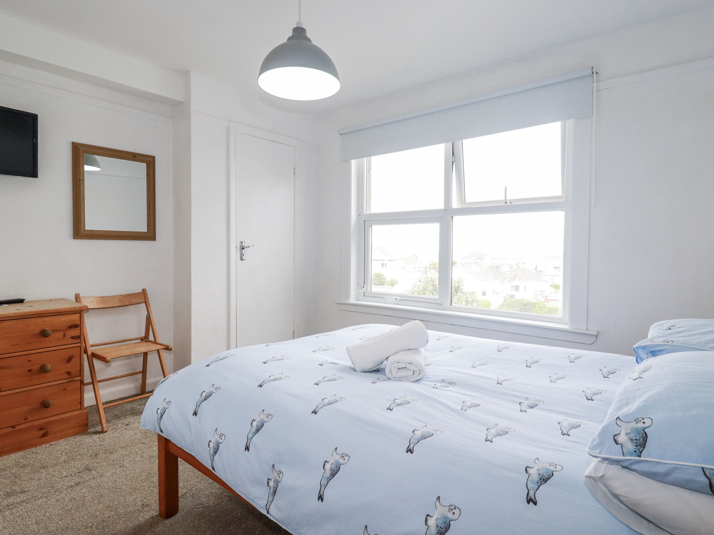 A bedroom with a bed, a wooden chair, a dresser, a mirror, and a window with blinds.