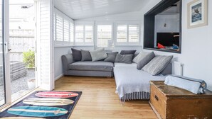 A cozy living room with a grey sofa, a wooden floor, and a surfboard rug.
