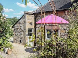 A stone building with a pink umbrella, surrounded by greenery and a gravel path. - Green Farm Cottage (Ashbourne)
