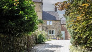 A stone building with a gravel path leading to a gated entrance. - Green Farm Cottage (Ashbourne)