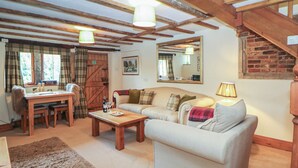 A cozy living room with a sofa, a coffee table, and a dining table. There is a wooden staircase and a large mirror on the wall. - Green Farm Cottage (Ashbourne)