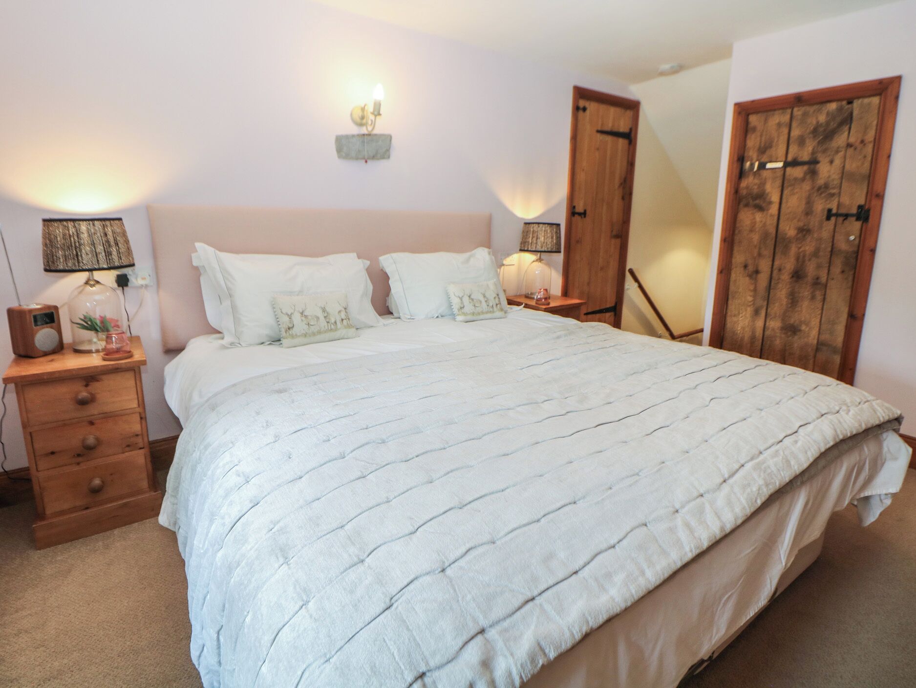 A bedroom with a large bed, two bedside tables with lamps, a dresser, and a wooden wardrobe.