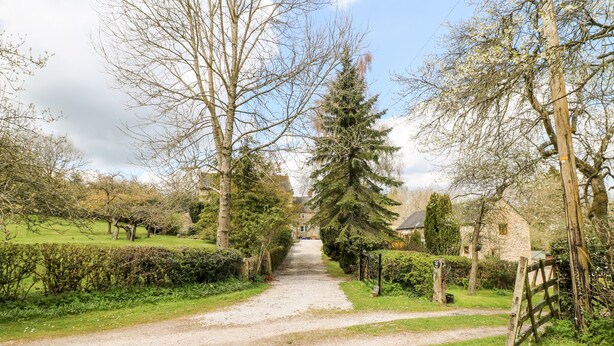 A rural pathway flanked by trees and hedges, leading to a stone building. - Green Farm Cottage (Ashbourne)