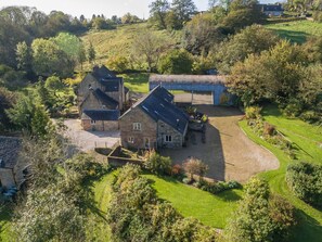 A stone farmhouse with a large barn, surrounded by lush greenery and rolling hills.