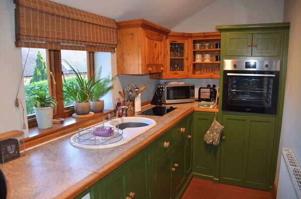 A kitchen with wooden cabinets, a microwave, an oven, a sink, and a window with plants.