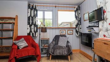 A cozy room with a red chair, a grey armchair, a wooden table, a TV, and a window with curtains.