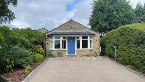 A stone house with a blue door, a gravel driveway, and surrounding greenery. - Hockerley Cottage (High Peak)