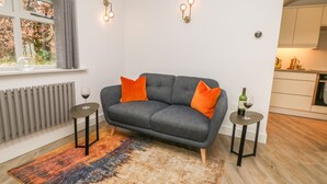 A modern living room with a grey sofa, orange cushions, a colorful rug, and two side tables with wine glasses. - Hockerley Cottage (High Peak)