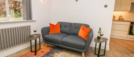 A modern living room with a grey sofa, orange cushions, a colorful rug, and two side tables with wine glasses.