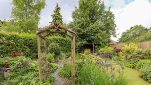Un jardin agrémenté d’une tonnelle en bois, d’un sentier en pierre et de diverses plantes à fleurs.