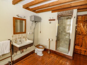 A bathroom with a wooden floor, a white sink with a wooden cabinet, a wooden toilet, a glass shower enclosure, and a wooden door. - Plosh House (Keswick)