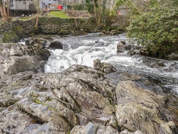 A rocky river with a stone wall and greenery.