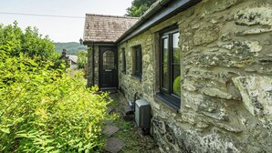 A stone building with a black door, windows, and a small garden area. - Tyn Y Ffynnon (Betws-Y-Coed)
