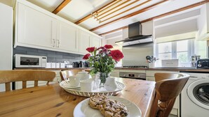 A kitchen with white cabinets, a wooden table, a coffee maker, a toaster, and a vase with flowers. - Tyn Y Ffynnon (Betws-Y-Coed)
