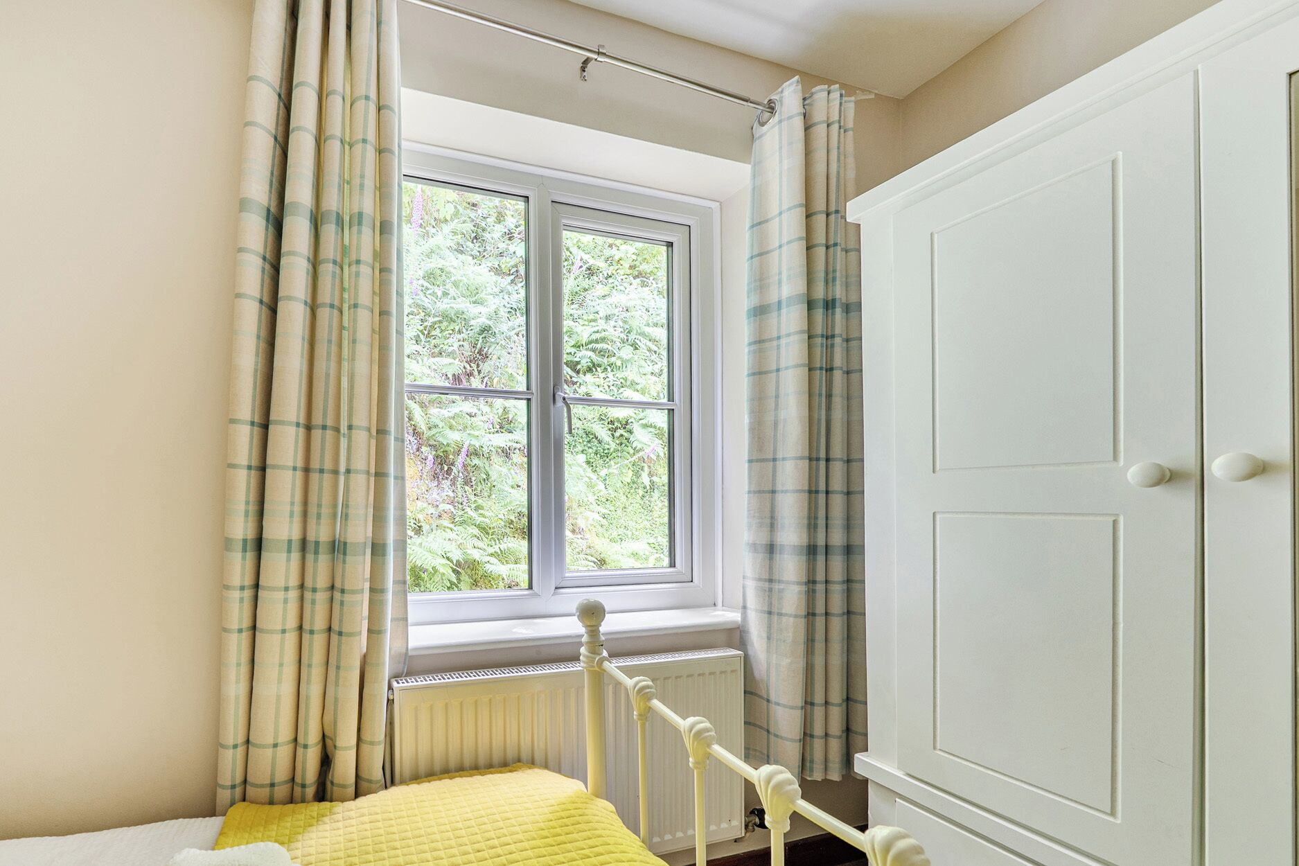 Une chambre avec un lit, une fenêtre avec des rideaux, un radiateur et une armoire blanche.