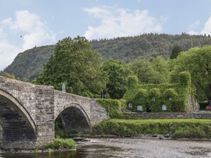 A stone bridge over a river with a forested hill in the background.