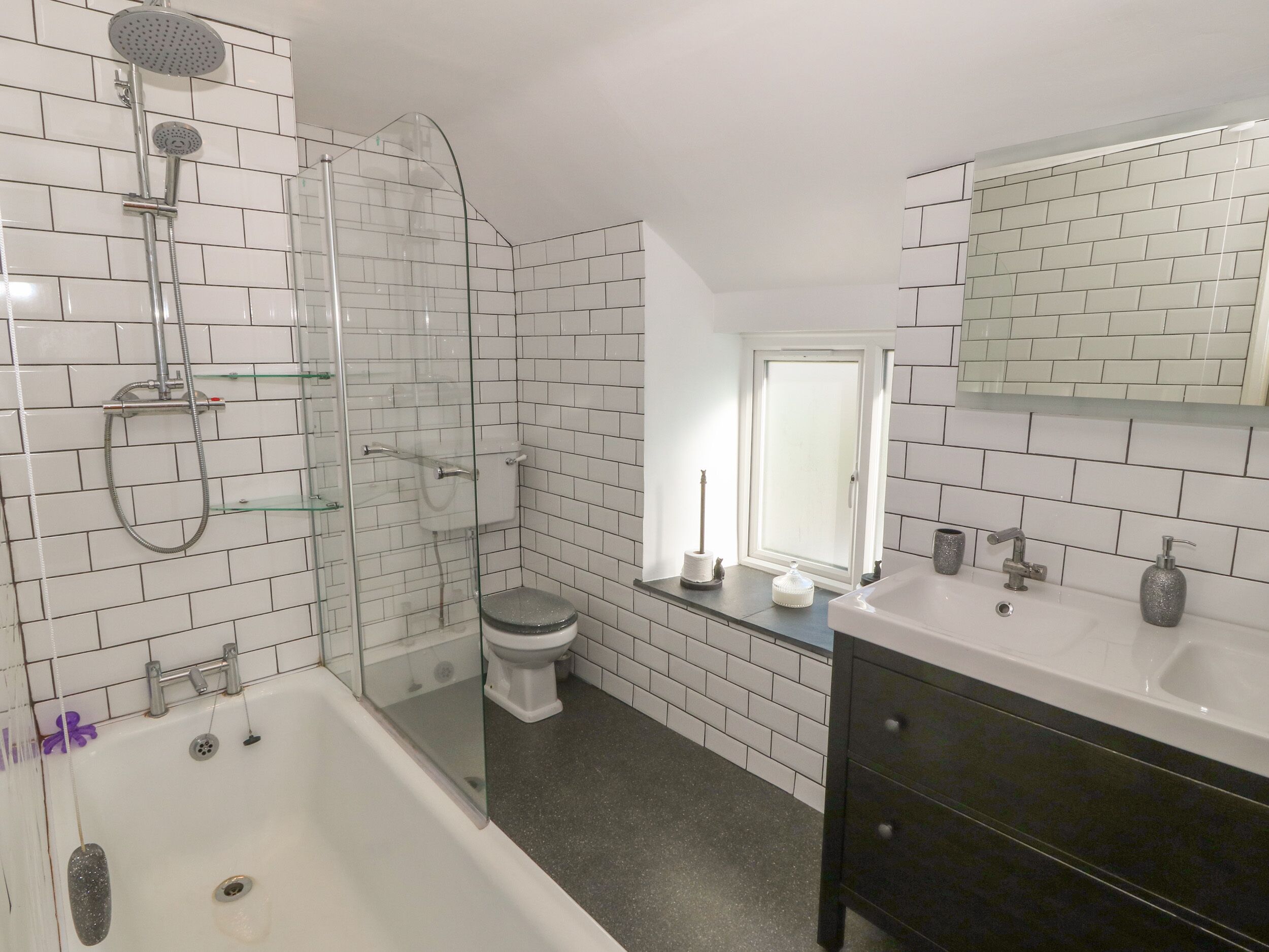 Un baño con azulejos blancos tipo metro, una cabina de ducha de vidrio, inodoro blanco, tocador con espejo y bañera.