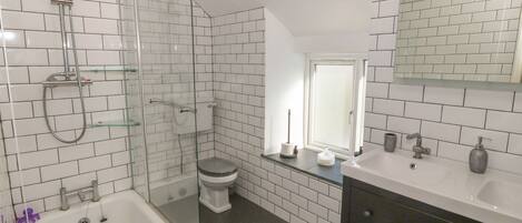 Un baño con azulejos blancos tipo metro, una cabina de ducha de vidrio, inodoro blanco, tocador con espejo y bañera.
